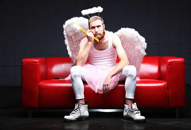 part of a humor series of tooth fairy or angel. This tooth fairy is looking bored and holding sitting on a red leather couch holding a giant tooth brush.