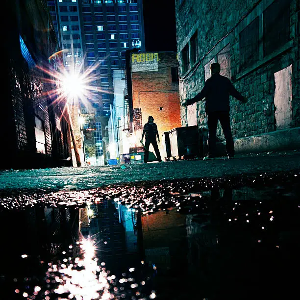 two dark figures face off on dark alley.