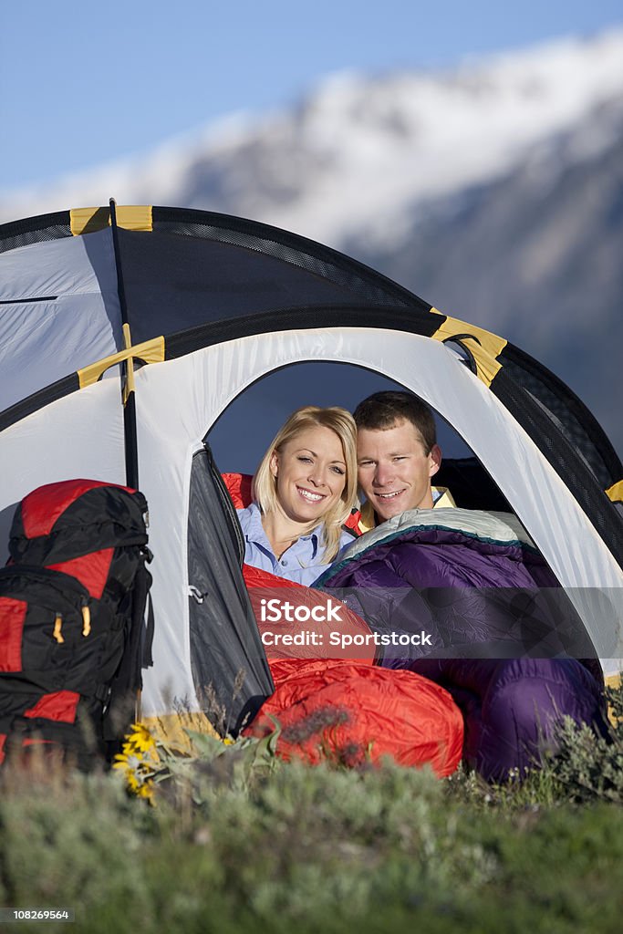 Young Couple Sitting Inside Small Tent In Mountains Young man and woman camping in the Rocky Mountains sitting in brightly colored tent. Camping Stock Photo