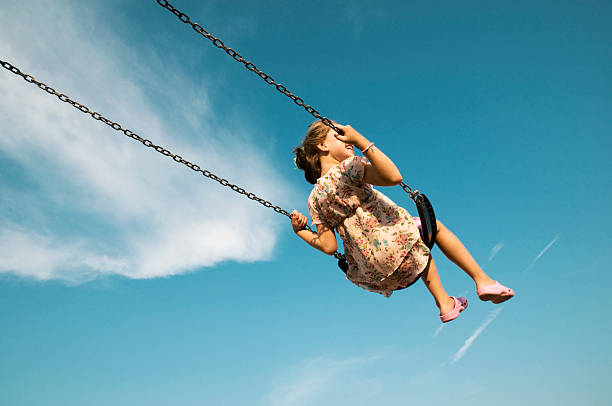 niña balanceo contra el cielo azul - parque infantil fotografías e imágenes de stock