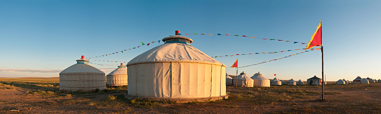 Warm sunlight illuminating the traditional yurts, prayer flags and vast open spaces of the Mongolian grasslands under panoramic blue skies. ProPhoto RGB profile for maximum color fidelity and gamut.