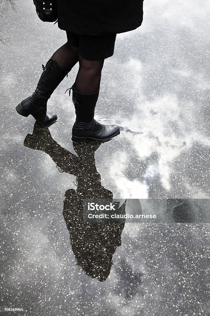 Młoda kobieta spaceru przez Kałuża w pochmurny dzień - Zbiór zdjęć royalty-free (But z cholewką)