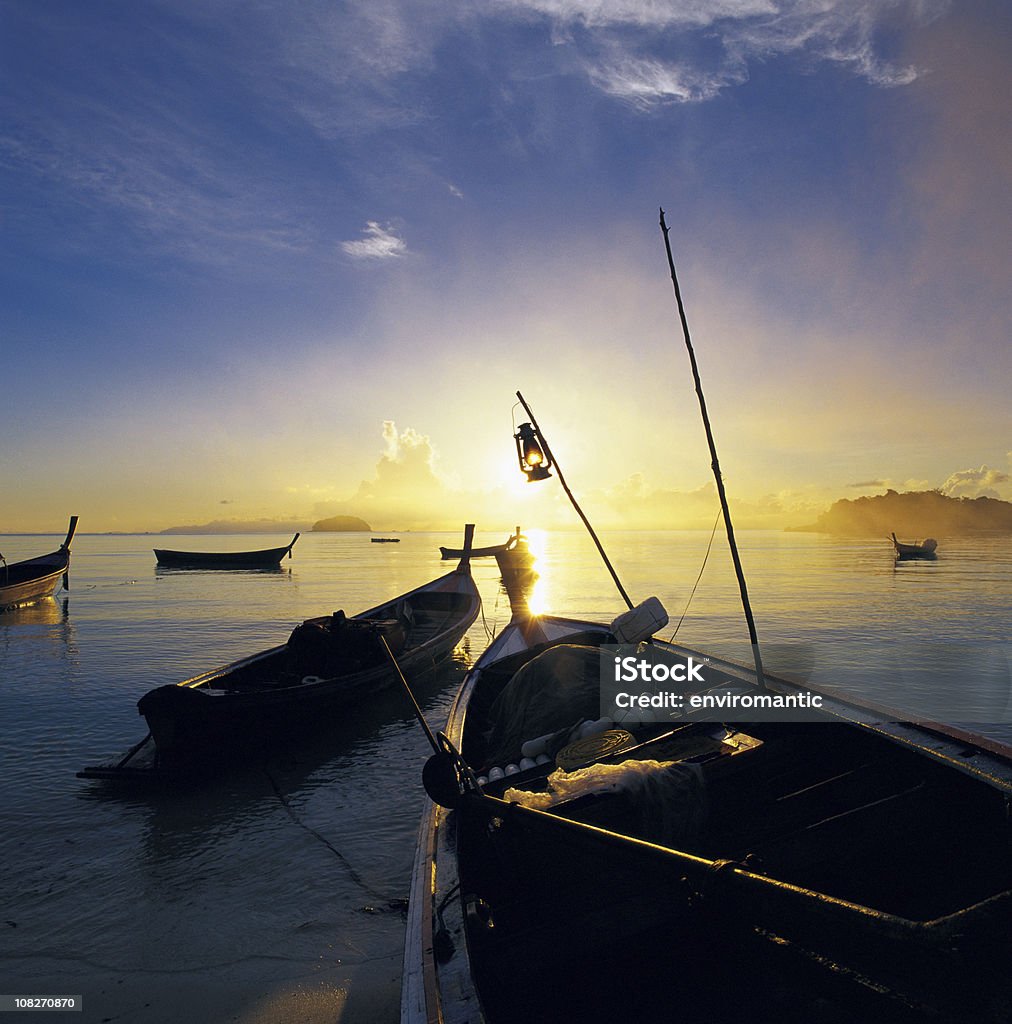 Fishing boats at sunrise. At sunrise, the sun shines across the sea from the horizon, silhouetting fishing boats moored at the shore, Satun Province, Thailand Southeast Asia.  Andaman Sea Stock Photo