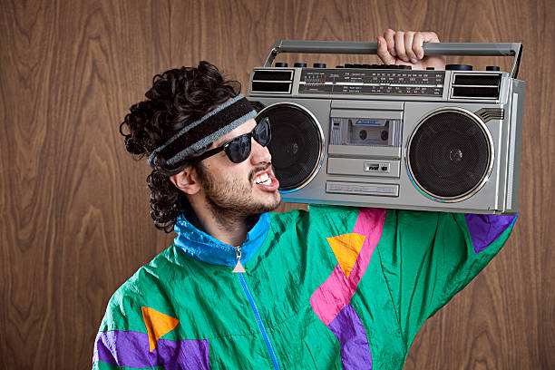 Fashion of the 1980's &amp; 90's With Boombox A hip funky young man with a mullet and fluorescent jump suit windbreaker.  Dark 80's style glasses cover his eyes as he sings along to his "ghetto blaster" boom box.  Wood paneled wall for copy space in the background. 1990s style stock pictures, royalty-free photos & images
