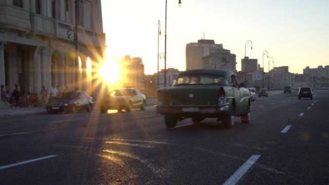 Golden hour sunset in old Havana with classic cars driving on waterfront street