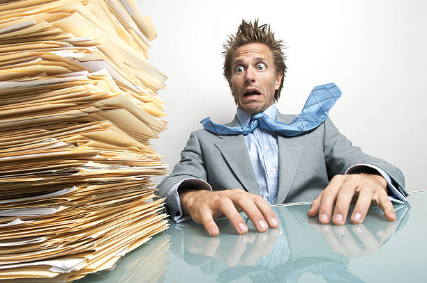 A white collar business man working in a retro 1980's style office sits at a desk piled with paperwork and documents.  He looks at the camera with a cheesy smile while making his sales pitch.