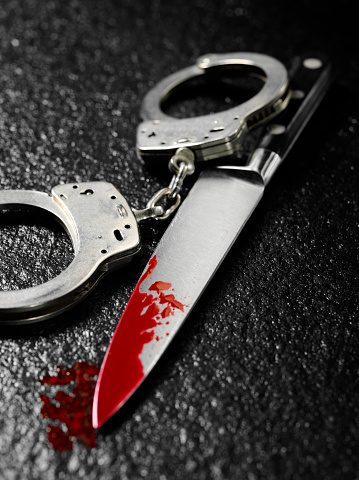 Knife and handcuffs on a dark stone background, knife crime with blood.