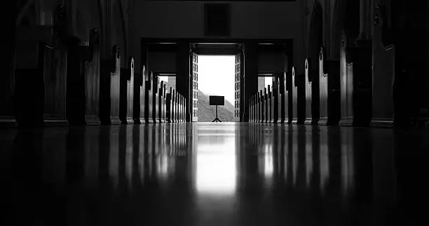 Black and white picture from inside an empty church looking toward the open exit door