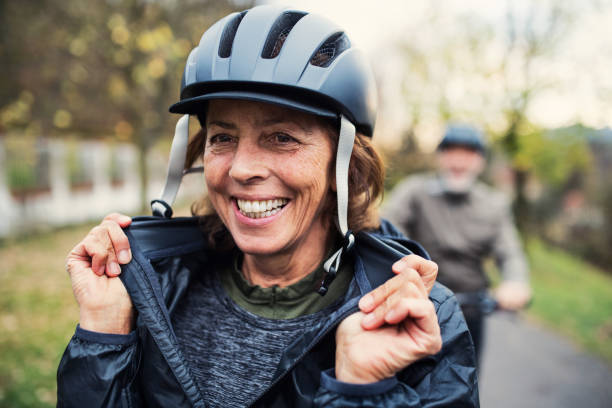Active senior couple with electrobikes standing outdoors on a road in park.