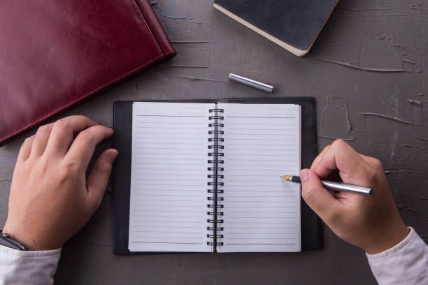 istock Top view of man hands writing on empty notebook with pen in office. Businessman working at office desk. Business concept. 1082721386