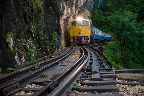 A train passes over the Krasae Viaduct at dusk near Kanchanaburi, Thailand.  This track is part of the infamous Death Railway, built during WWII. Passengers are looking out the windows.