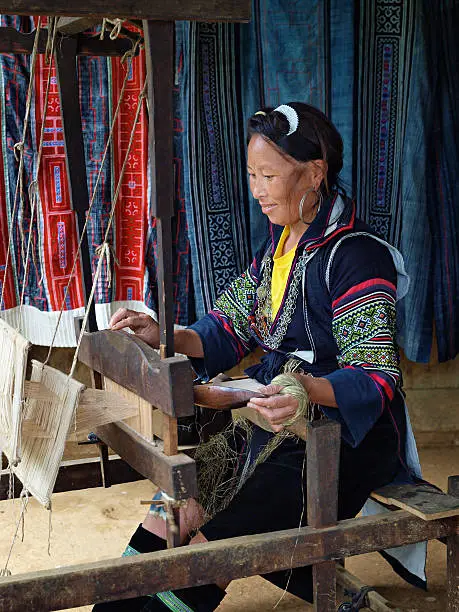 An woman of the Black H'mong Hilltribe (North Vietnam) dressed in traditional ethnic costume operating a weaving loom.