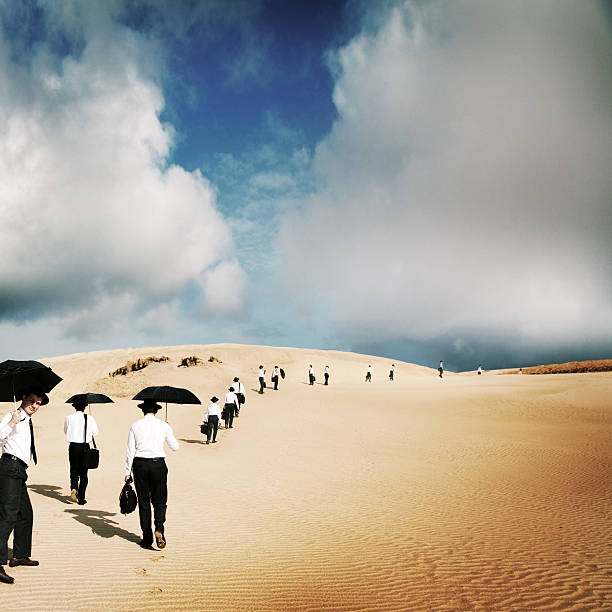 A group of people climbs up a dune while some others sit on the edge of it. The deep blue sky contrasts with the sand