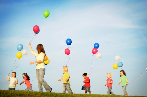Color photo of children walking and running with balloons.