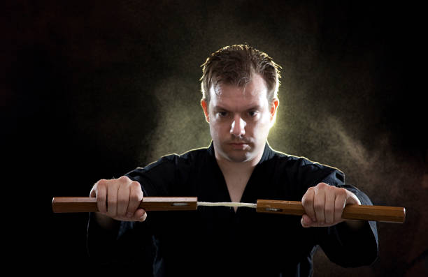 karaté homem segurando nunchucks em fundo preto - nunchaku imagens e fotografias de stock