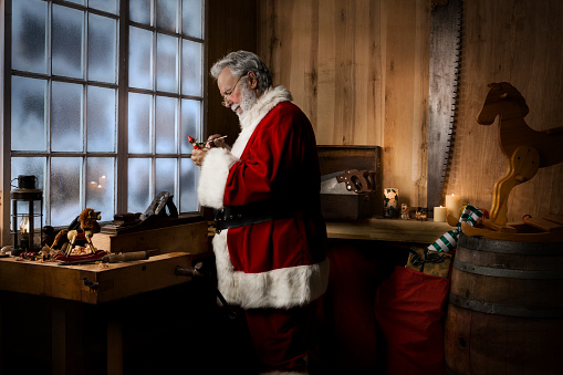 Santa Claus painting a toy in his workshop, lit with lantern and candles. Copy space. CLICK FOR SIMILAR IMAGES OR LIGHTBOX WITH MORE SEASONAL IMAGES.