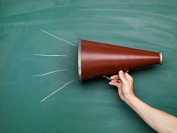 A brown megaphone in front of a green chalkboard with lines stock photo