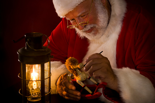 Santa Claus painting a toy by a lit lantern. Edited for classic, film-like feel. CLICK FOR SIMILAR IMAGES OR LIGHTBOX WITH MORE SEASONAL IMAGES.