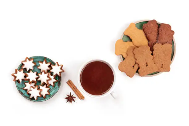 A photo of Zimsterne and Spekulatius, traditional Christmas cookies, shot from the top on a white background with hot chocolate, spices, and copy space