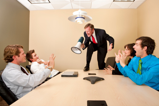 Crazy boss standing on conference table and yelling at employees with megaphone.