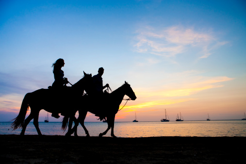 Rear view of a woman horseback riding along the beach in the North East of England. The scene is tranquil and calm. The horse is leaving footprints in the sand.