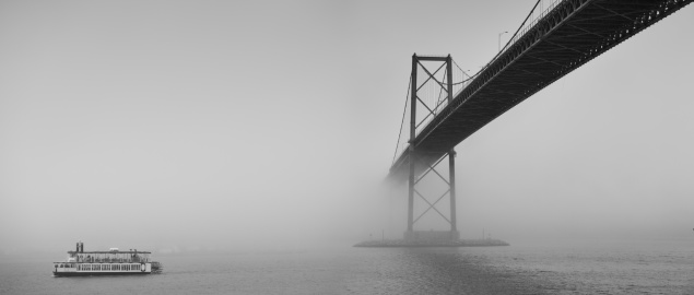 Ferry boat crossing the East River in heavy fog under the Brooklyn Bridge.