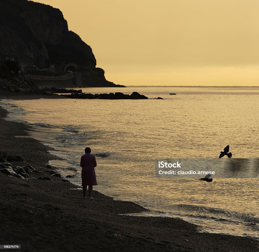 Edad mujer caminando en la playa al atardecer. Sepia tono - Foto de stock de Aire libre libre de derechos