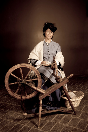 full-body portrait of an attractive woman dressed in pioneer clothing spinning yarn on an authentic machine.
