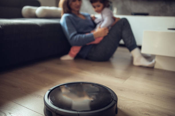 istock Robotic Vacuum Cleaner Cleaning Floor While Mother and Daughter Relaxing 1082750324