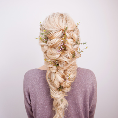 Back view of an elegant trendy hairstyle, interlacing curls and decorating with flower petals. Beautiful and well-groomed blonde hair