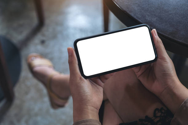 istock Mockup image of woman's hands holding black mobile phone with blank white screen horizontally for watching while sitting in cafe 1082812054