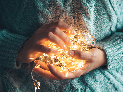 lights in the palms. Women's hands holding a garland. Girl in a blue sweater with Christmas lights in her hands, warm Christmas mood, soft focus