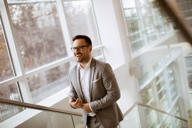 istock Happy businessman dressed in suit standing  in modern office  and using tablet 1082833892