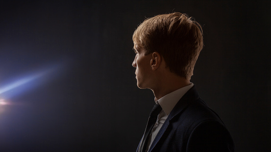 Profile of a brooding young man in a business suit. Portrait of a businessman on a dark background