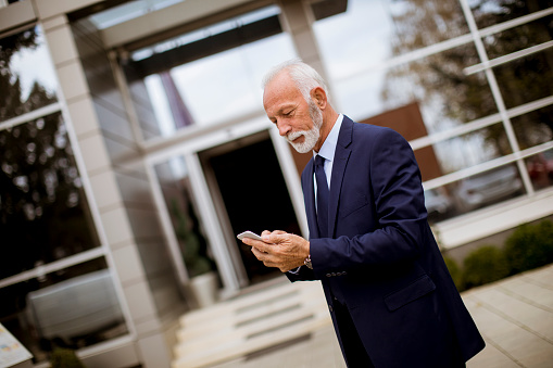Portrait of senior businessman using mobile phone in front of office building