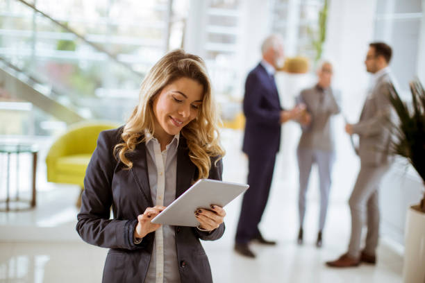 istock Young businesswoman using with tablet in office while other business people talking in background 1082841784