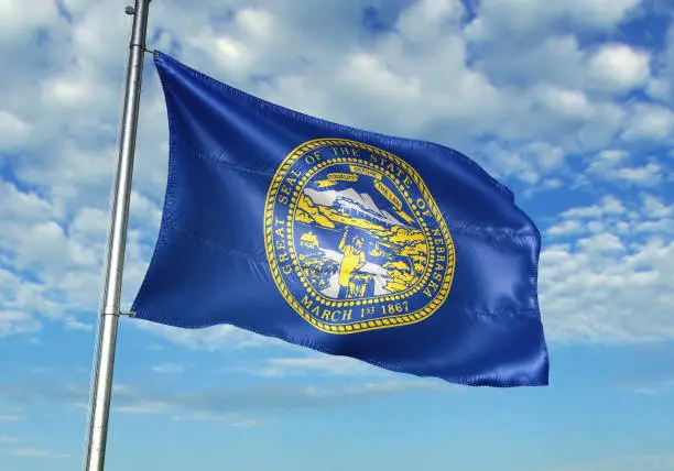 Nebraska state of United States flag on flagpole waving cloudy sky background realistic 3d illustration