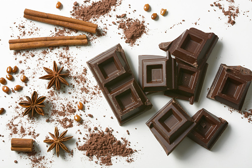 pieces of chocolate, cinnamon, star anise and cocoa powder on the white background - closeup