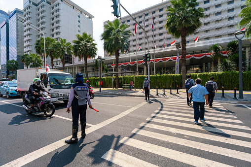 Jakarta, Indonesia - August 20, 2018:  view showing traffic enforcer stops the motorcycles, van and cars while pedestrian crossing in pedestrian lane in Jakarta street