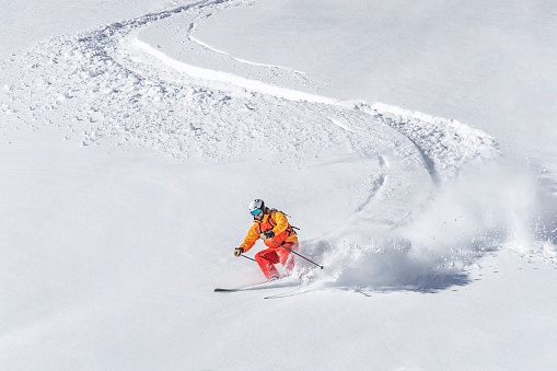 One adult freeride skier skiing downhill through deep powder snow