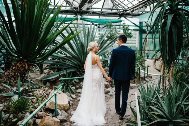 retrato o noivo no terno do casamento e a noiva com o vestido vão voltar no botânico jardim verde cheio de vegetação. cerimônia de casamento. recém-casados. - local desportivo - fotografias e filmes do acervo