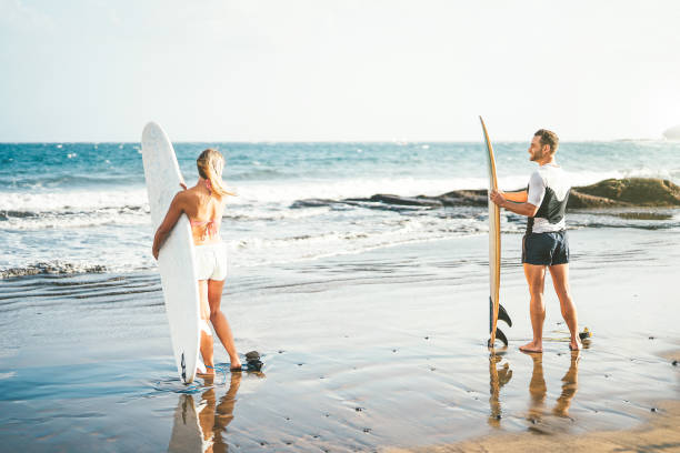 junges paar surfer stehen am strand mit surfbrettern surfen auf hohe wellen - sportliche leute, die spaß an einem surftag - extreme sport, beziehung und jugend lifestyle-konzept wird vorbereitet - surfing men hawaii islands wave stock-fotos und bilder