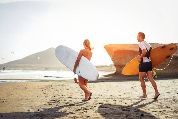 couple de surfeurs exécutant ensemble avec des planches de surf sur la plage au coucher du soleil - sporty amis s’amuser aller au surf - voyage, vacances, concept lifestyle sport - surfing men hawaii islands wave photos et images de collection