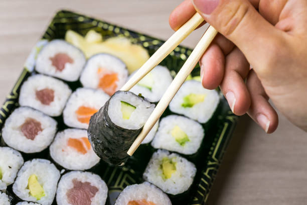 istock Hand using chopsticks pick Sushi and Sashimi rolls on a black stone slatter. Fresh made Sushi set with salmon, prawns, wasabi and ginger. Traditional Japanese cuisine 1082891442
