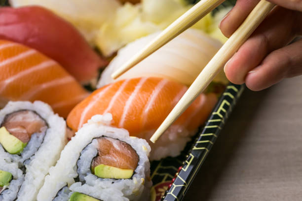 istock Hand using chopsticks pick Sushi and Sashimi rolls on a black stone slatter. Fresh made Sushi set with salmon, prawns, wasabi and ginger. Traditional Japanese cuisine 1082891582