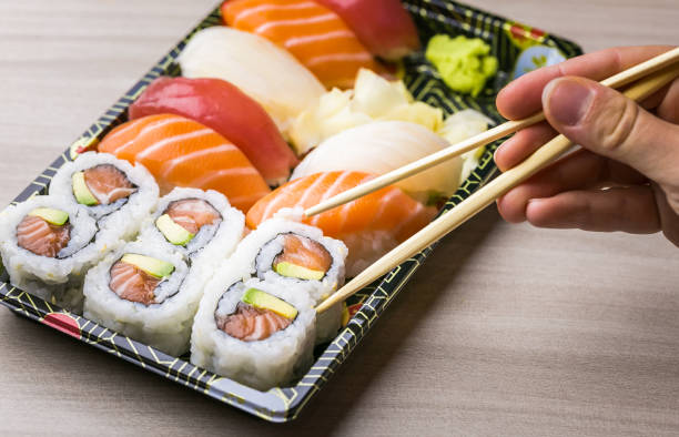 istock Hand using chopsticks pick Sushi and Sashimi rolls on a black stone slatter. Fresh made Sushi set with salmon, prawns, wasabi and ginger. Traditional Japanese cuisine 1082891788