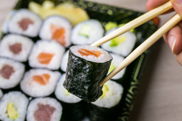 istock Hand using chopsticks pick Sushi and Sashimi rolls on a black stone slatter. Fresh made Sushi set with salmon, prawns, wasabi and ginger. Traditional Japanese cuisine 1082891954