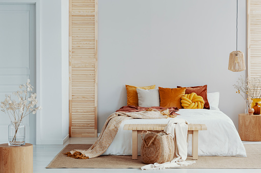 istock Marrón y naranja almohadas en una cama blanca natural dormitorio interior con lámpara de mimbre y madera mesita de noche con florero 1082907946
