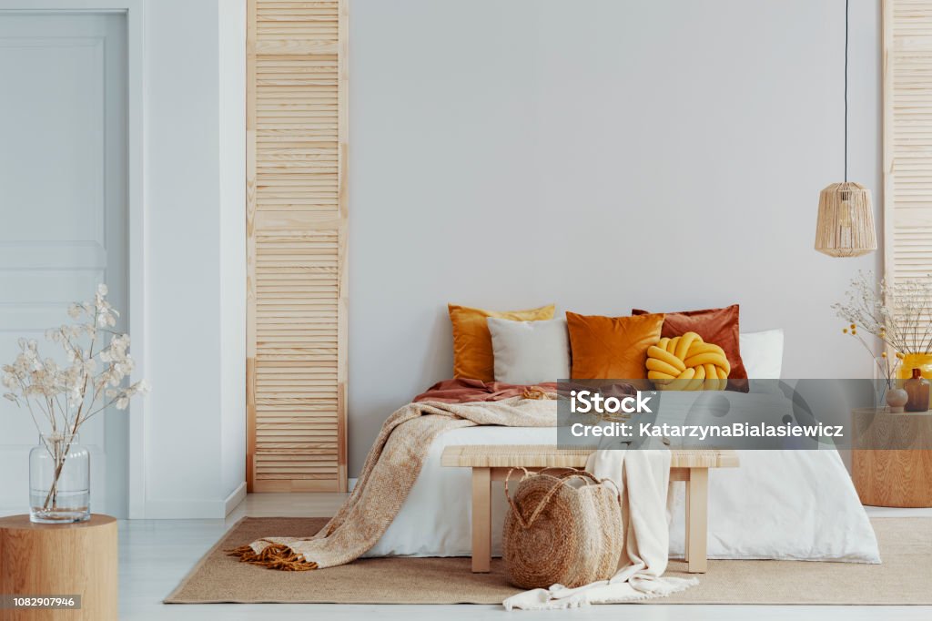 Brown and orange pillows on white bed in natural bedroom interior with wicker lamp and wooden bedside table with vase - Royalty-free Quarto de Dormir Foto de stock