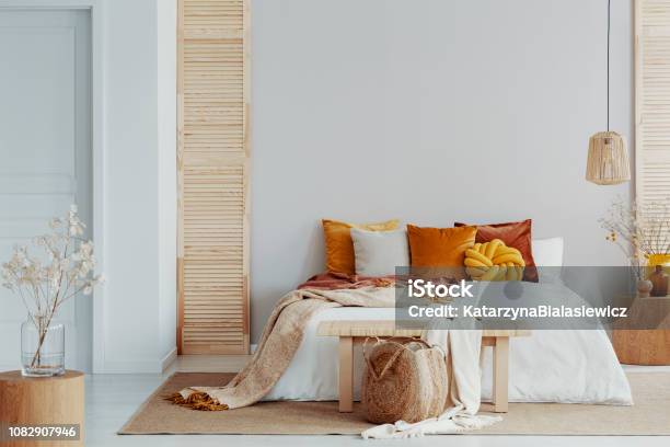 Brown And Orange Pillows On White Bed In Natural Bedroom Interior With Wicker Lamp And Wooden Bedside Table With Vase - Fotografias de stock e mais imagens de Quarto de Dormir